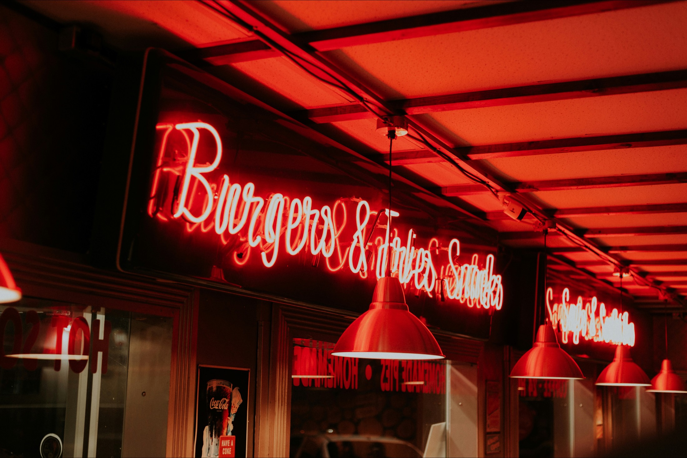 A red neon 'Burgers & Fries' sign glowing over a diner counter