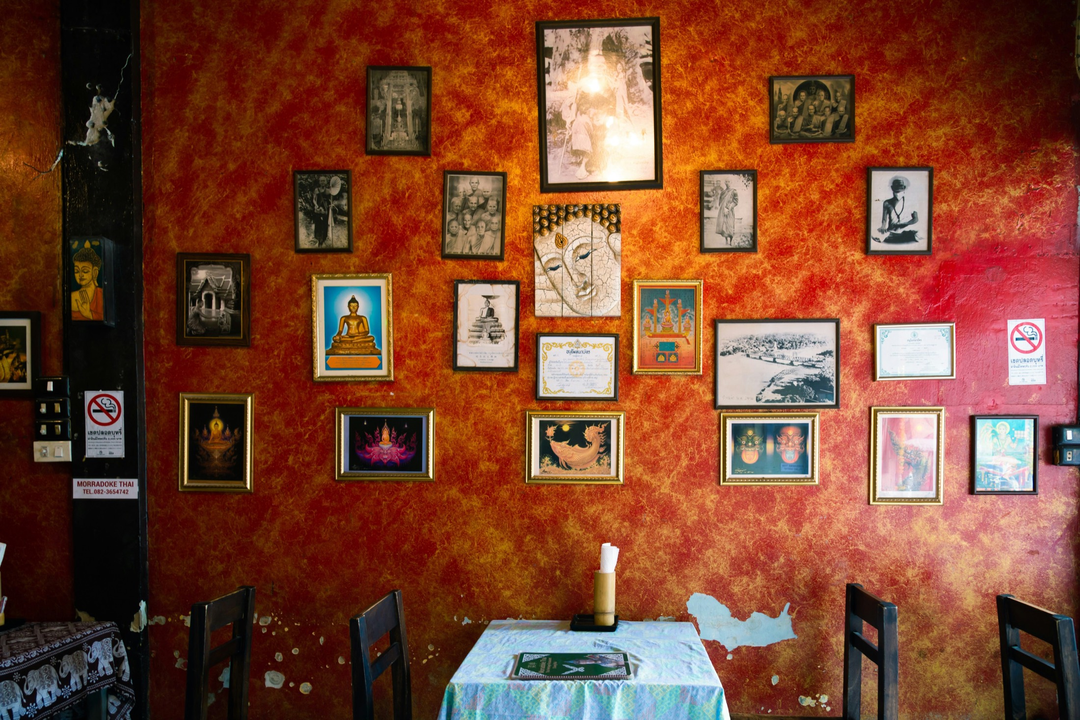 A wall of framed Buddha images and Thai art above a table in a Thai restaurant